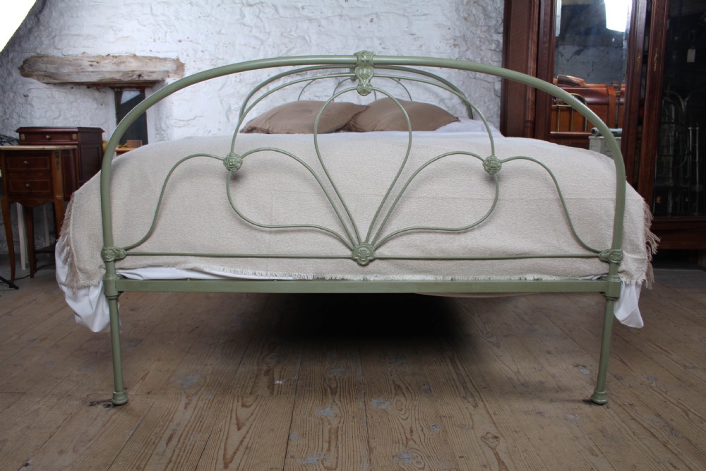 A green painted iron bedstead featuring arched headboard and footboard frames with decorative looped ironwork and cast medallions. View III