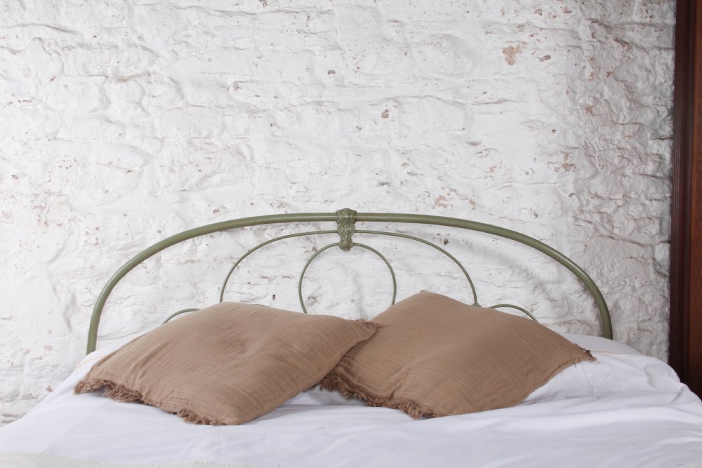 A green painted iron bedstead featuring arched headboard and footboard frames with decorative looped ironwork and cast medallions. View VI