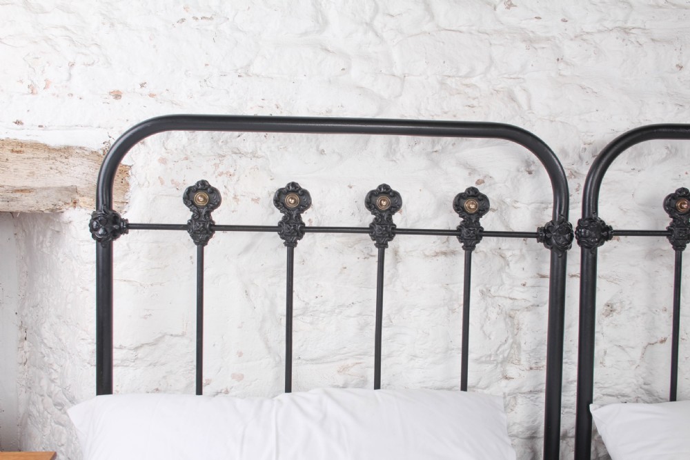 A pair of black wrought iron French single bed frames featuring vertical spindles with cast decorative rosettes and no footboards. View V