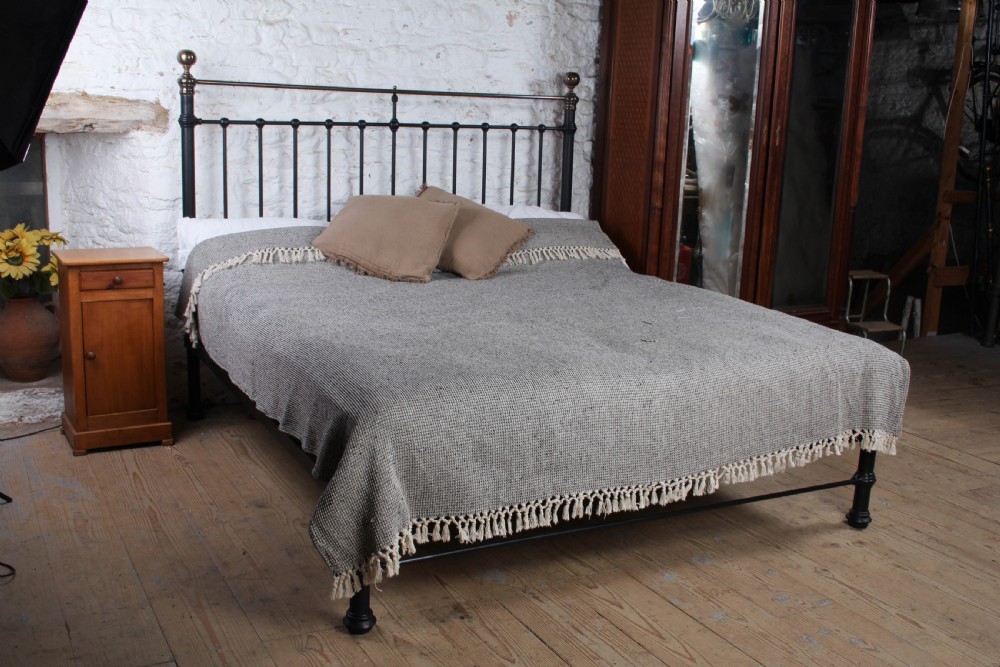 A super king size black iron bed frame featuring vertical spindles, a brass top rail, and round brass finials.
