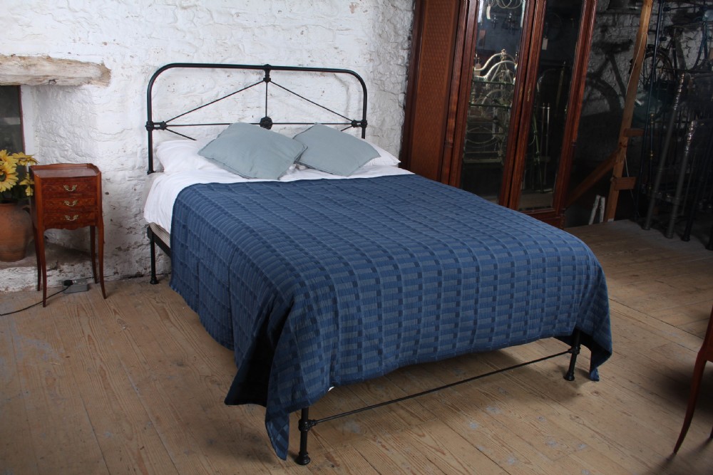 A Victorian black iron king-size bedstead featuring a rounded headboard frame decorated with geometric Celtic strapwork and cast iron bosses.