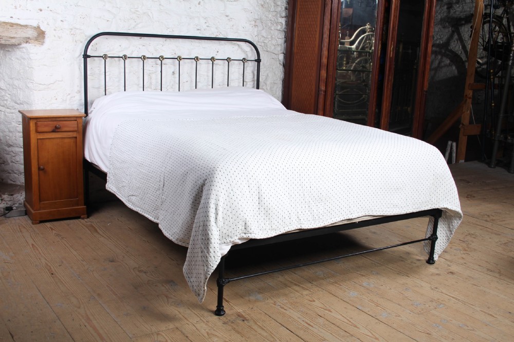 A king size black iron bed frame featuring a spindle headboard with brass roundels and a low foot end.