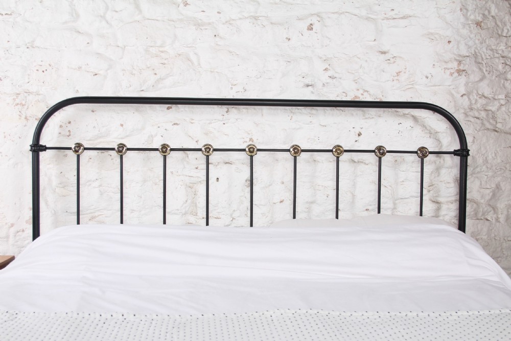 A king size black iron bed frame featuring a spindle headboard with brass roundels and a low foot end. View II