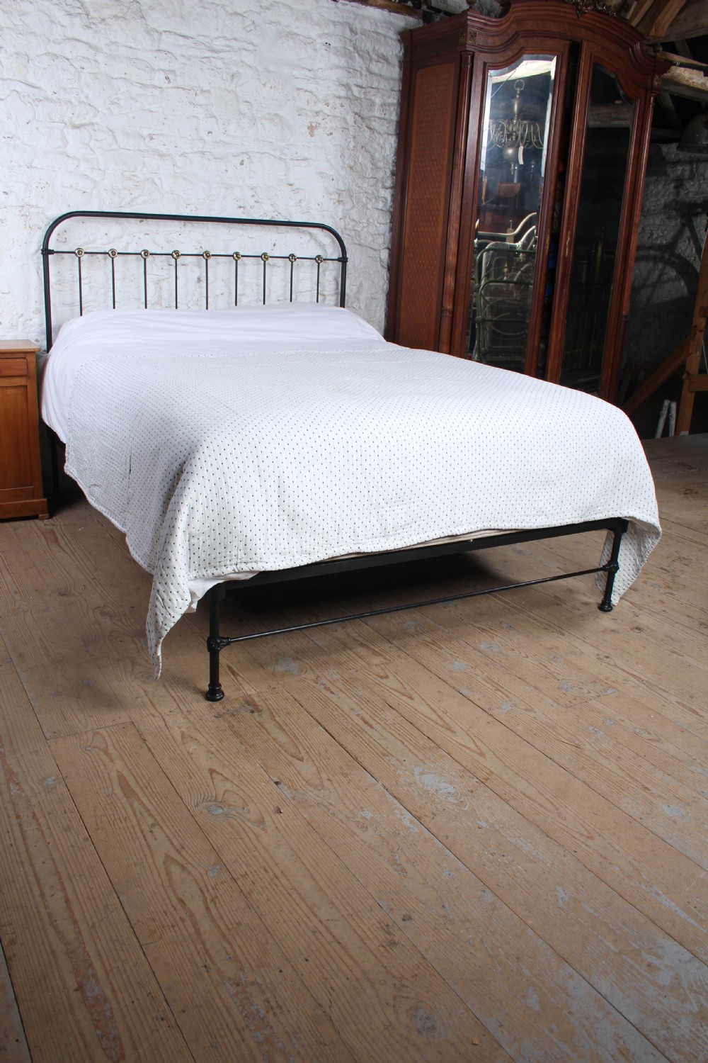 A king size black iron bed frame featuring a spindle headboard with brass roundels and a low foot end. View IV