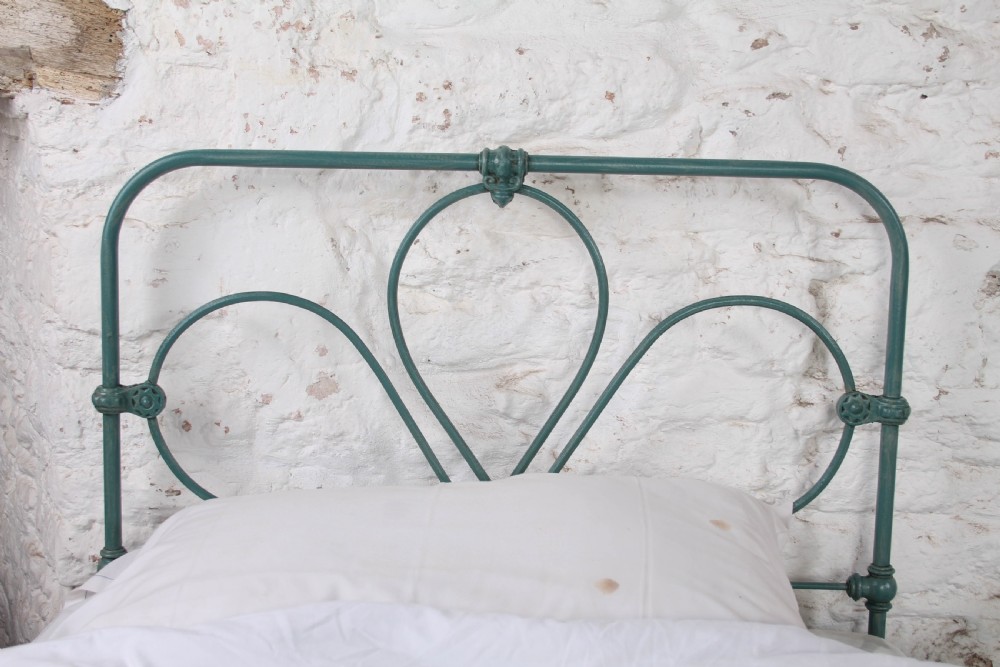 A pair of green painted iron single bed frames featuring scrolled Celtic heart motifs on the headboards and low open ends. View III