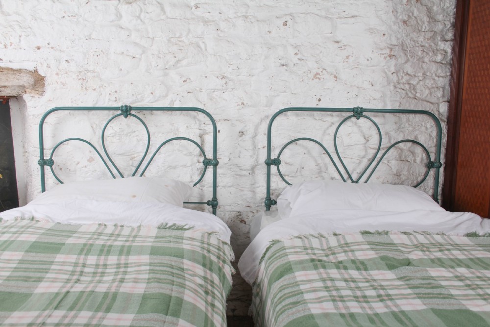 A pair of green painted iron single bed frames featuring scrolled Celtic heart motifs on the headboards and low open ends. View VI