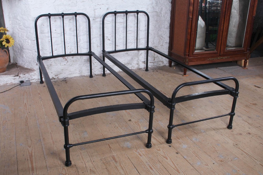 A pair of black painted tubular metal single bed frames featuring simplified vertical headboard spindles.
