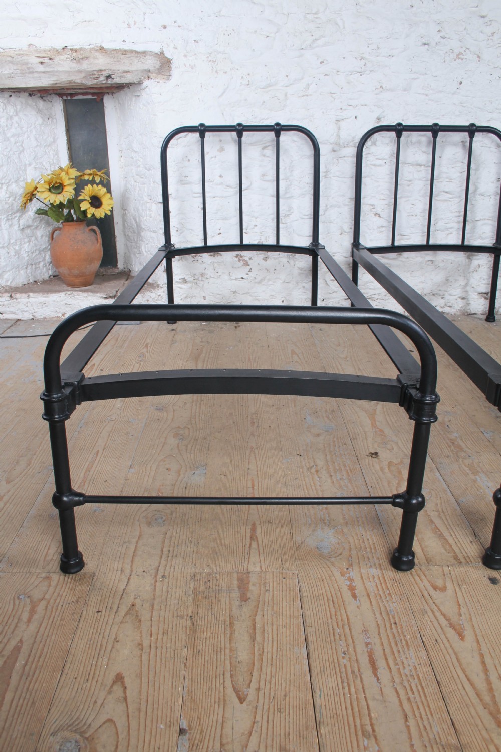 A pair of black painted tubular metal single bed frames featuring simplified vertical headboard spindles. View II
