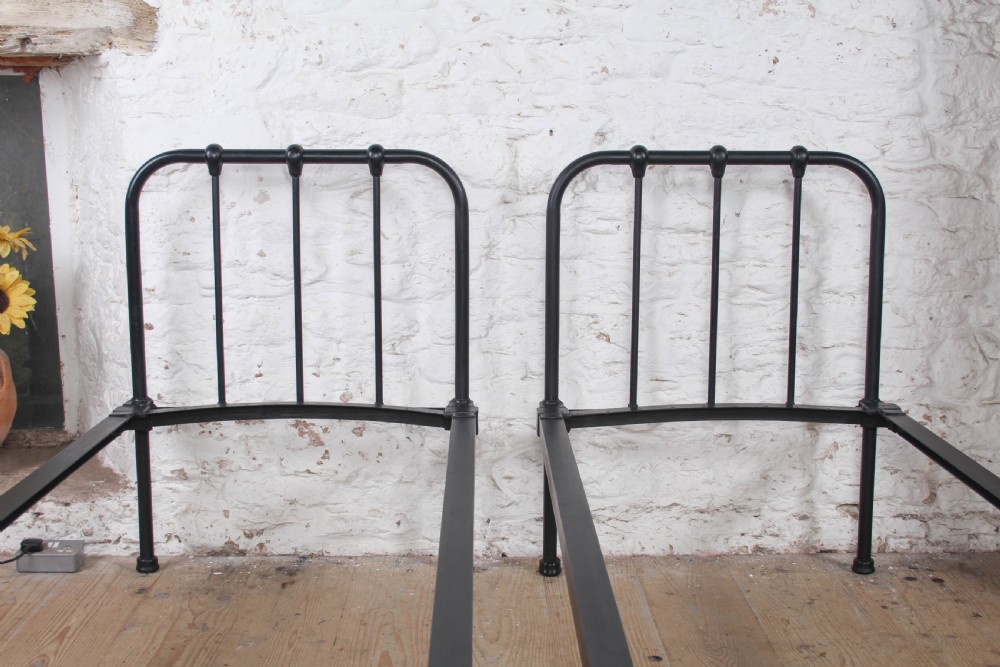 A pair of black painted tubular metal single bed frames featuring simplified vertical headboard spindles. View III