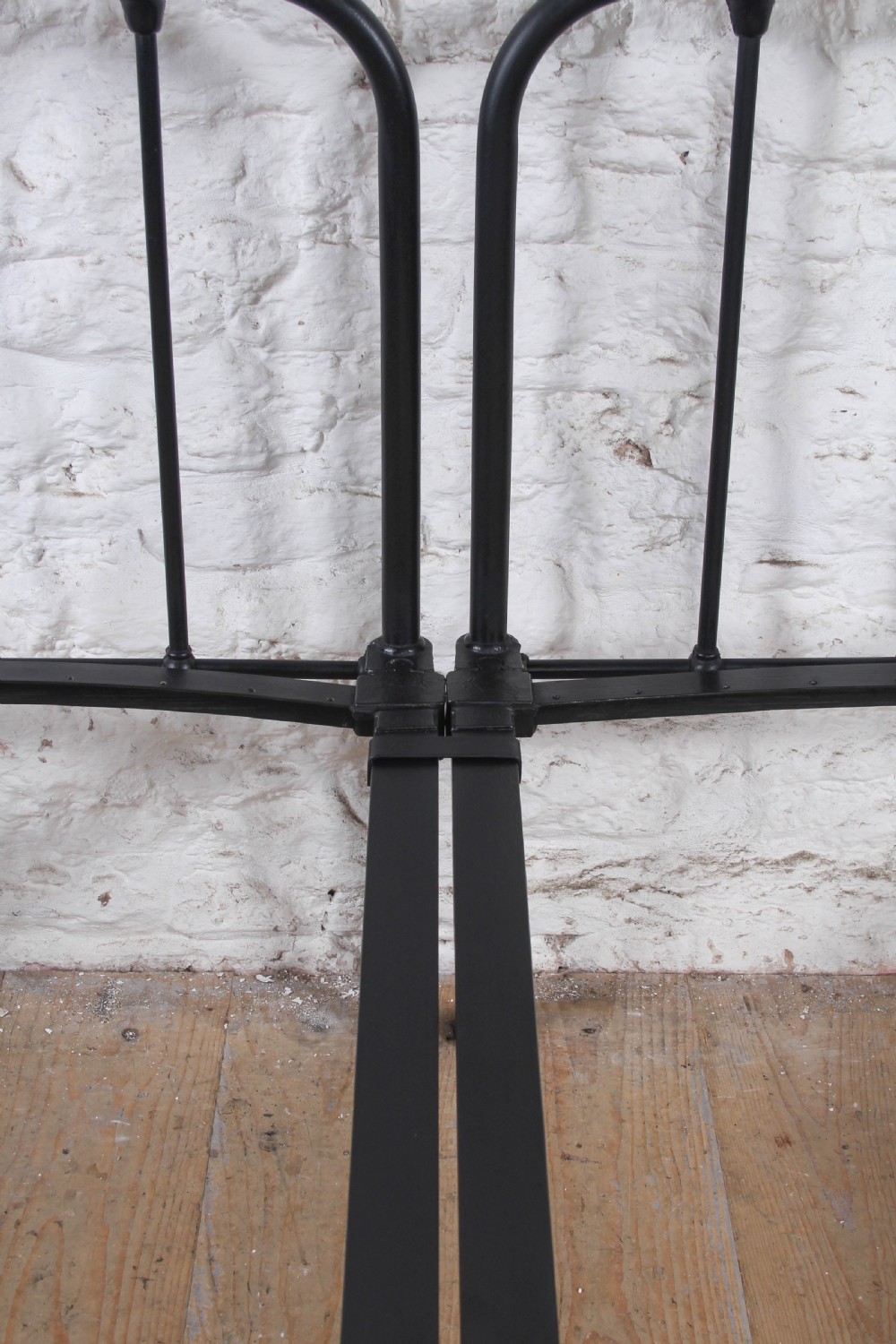 A pair of black painted tubular metal single bed frames featuring simplified vertical headboard spindles. View VI