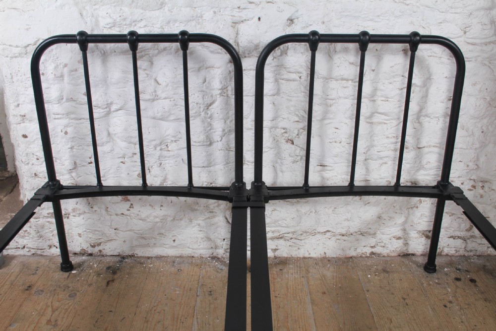 A pair of black painted tubular metal single bed frames featuring simplified vertical headboard spindles. View VII