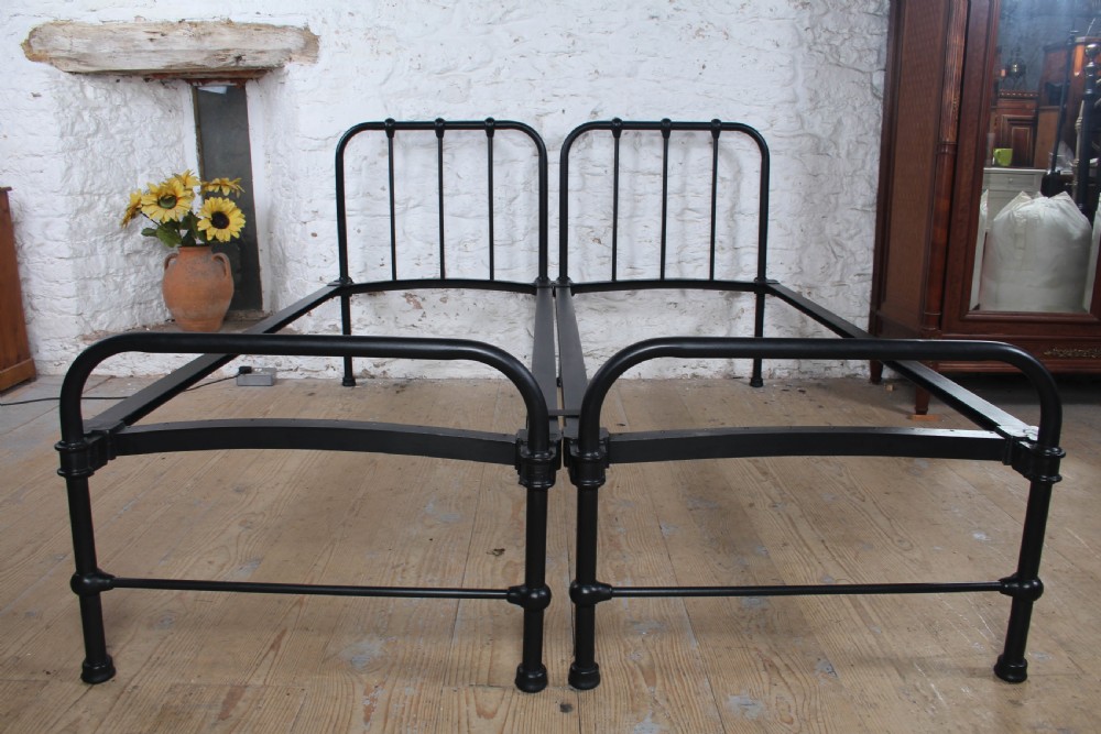 A pair of black painted tubular metal single bed frames featuring simplified vertical headboard spindles. View IX