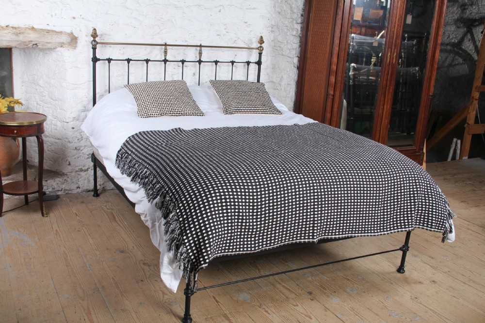 A Victorian black iron king-size bed frame featuring vertical headboard spindles, a brass top rail, decorative brass finials, and a low foot end.
