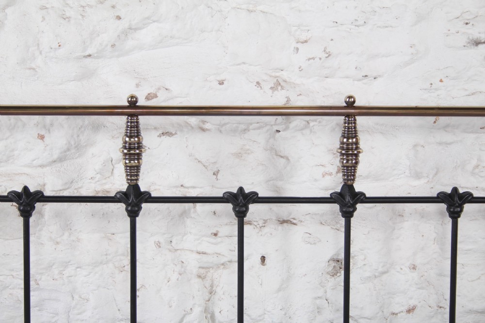 A Victorian black iron king-size bed frame featuring vertical headboard spindles, a brass top rail, decorative brass finials, and a low foot end. View IV