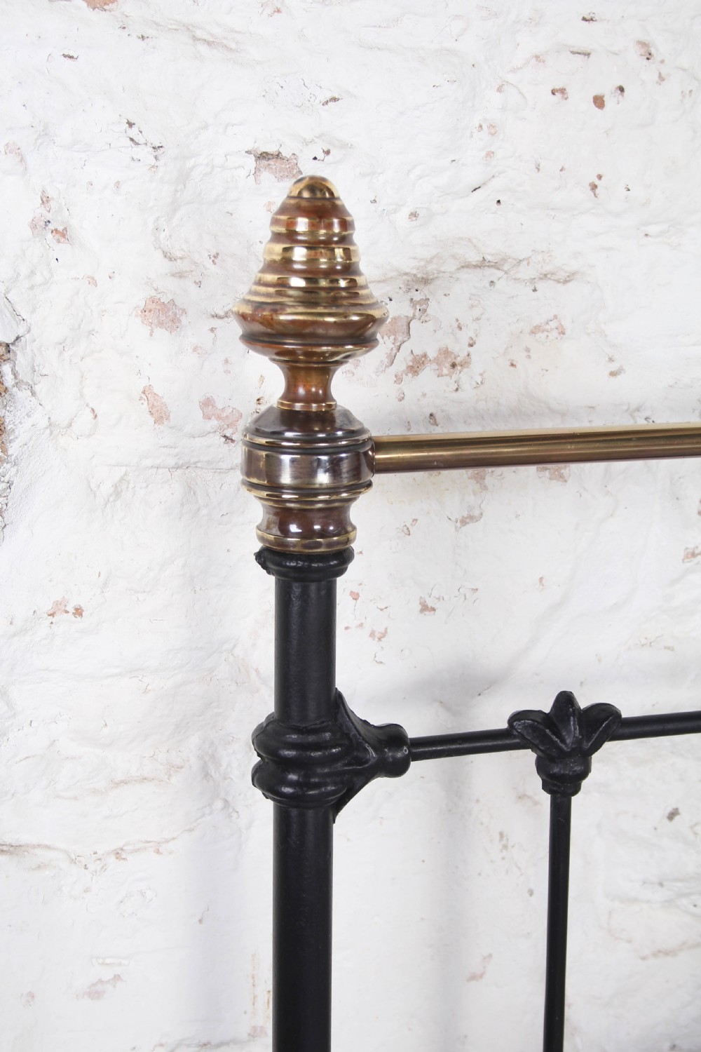 A Victorian black iron king-size bed frame featuring vertical headboard spindles, a brass top rail, decorative brass finials, and a low foot end. View VI