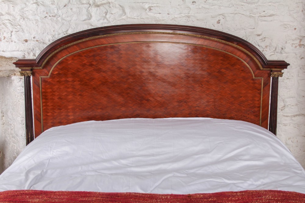 A French king-size bed frame featuring mahogany and fruitwood geometric parquetry inlay, arched headboard, brass trim, and fluted corner posts. View II