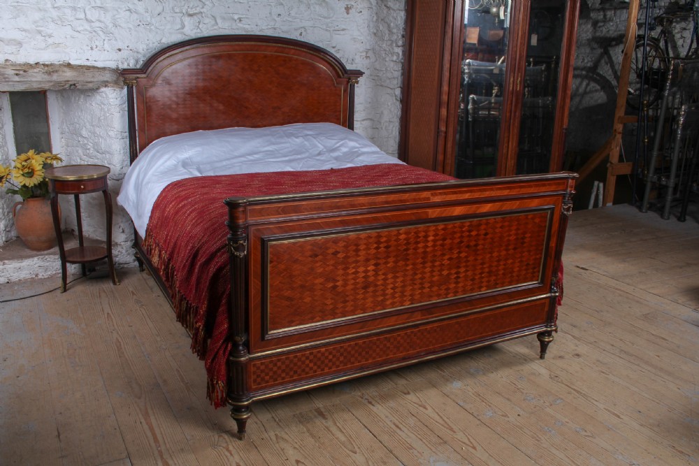 A French king-size bed frame featuring mahogany and fruitwood geometric parquetry inlay, arched headboard, brass trim, and fluted corner posts. View III
