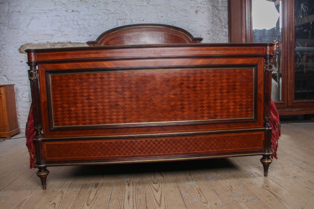 A French king-size bed frame featuring mahogany and fruitwood geometric parquetry inlay, arched headboard, brass trim, and fluted corner posts. View V