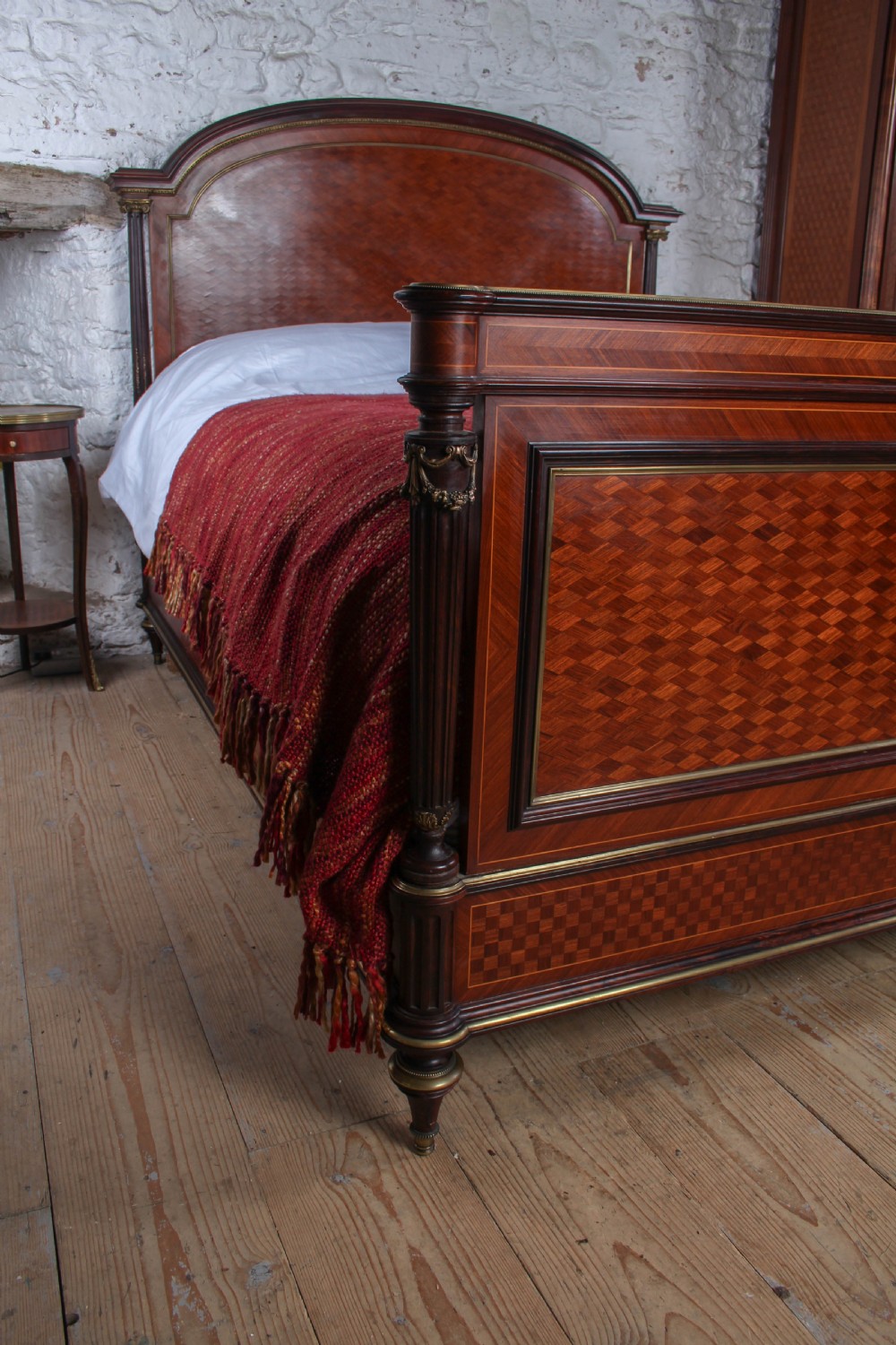 A French king-size bed frame featuring mahogany and fruitwood geometric parquetry inlay, arched headboard, brass trim, and fluted corner posts. View VI