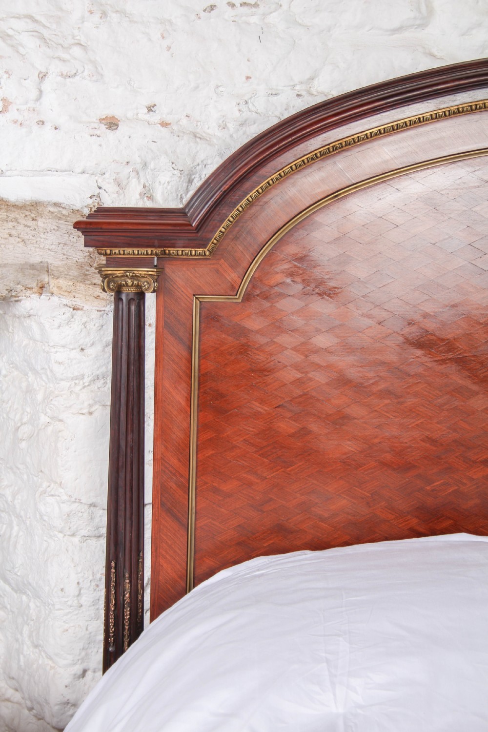 A French king-size bed frame featuring mahogany and fruitwood geometric parquetry inlay, arched headboard, brass trim, and fluted corner posts. View VIII