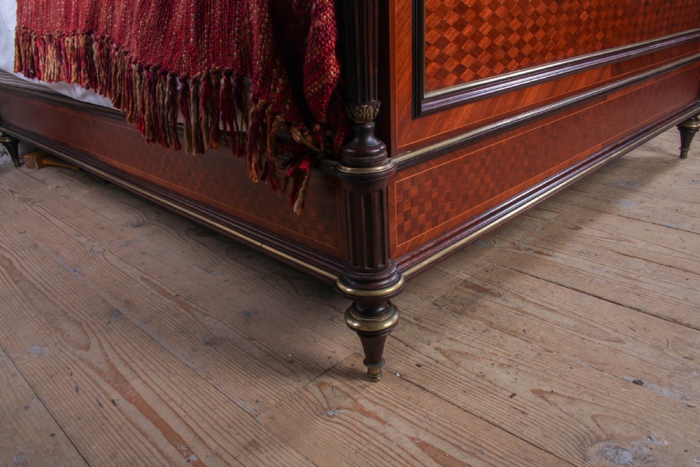 A French king-size bed frame featuring mahogany and fruitwood geometric parquetry inlay, arched headboard, brass trim, and fluted corner posts. View X