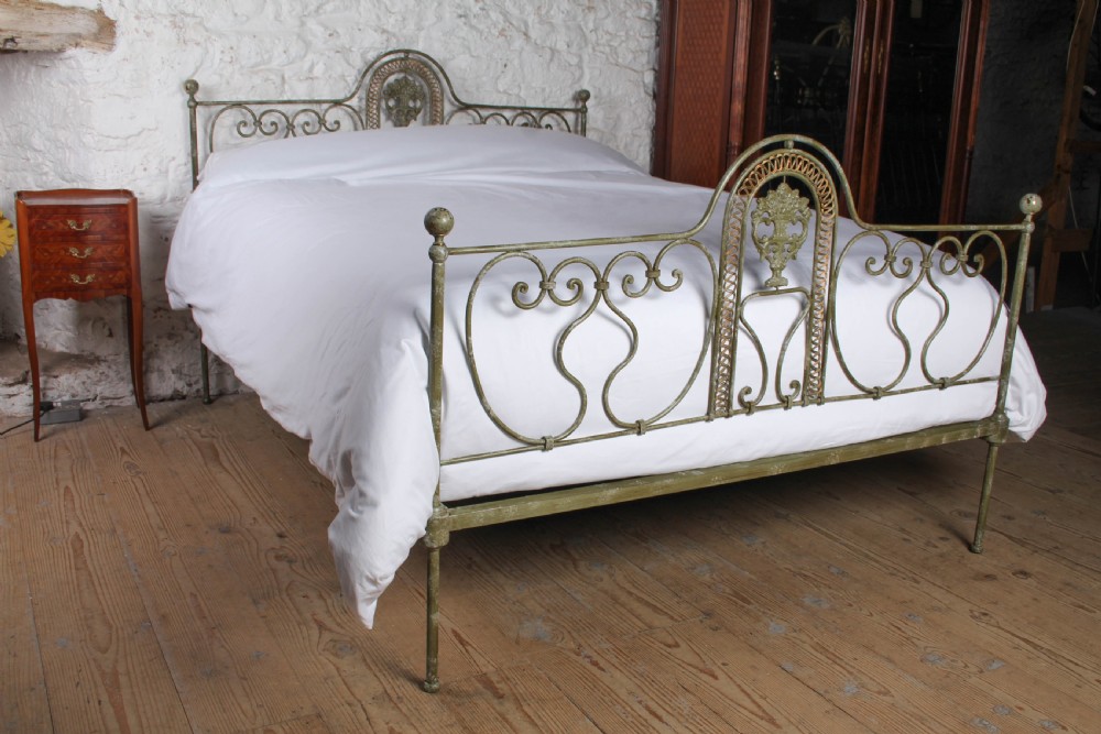 A king-size Portuguese wrought iron bed frame featuring an ornate arched headboard and footboard with central decorative medallions and a distressed green paint finish.