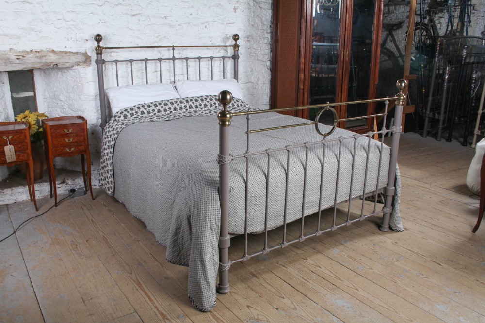 A Victorian cast iron and brass king size bedstead featuring vertical spindles, decorative brass finials, and a grey painted frame.