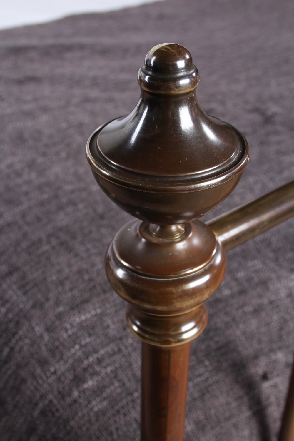 A king-size French brass bedstead featuring vertical metal spindles topped with circular ring motifs and decorative urn finials on four corner posts. View IV