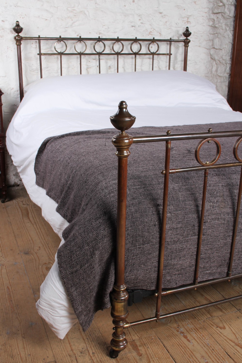 A king-size French brass bedstead featuring vertical metal spindles topped with circular ring motifs and decorative urn finials on four corner posts. View VII