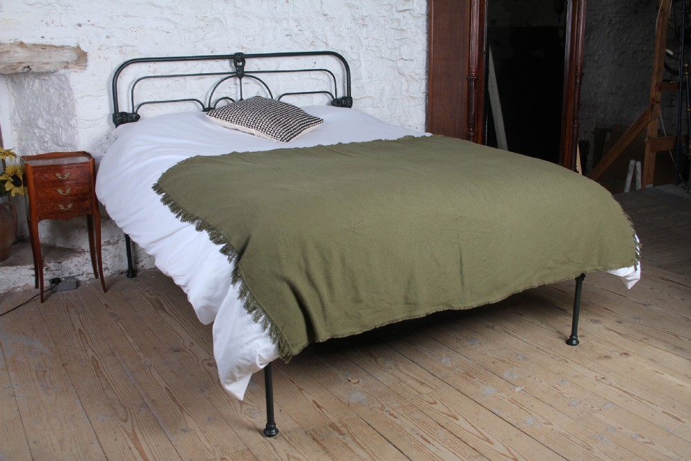 An antique king-size black cast iron bed frame featuring a curved tubular headboard with central cast details and no footboard.
