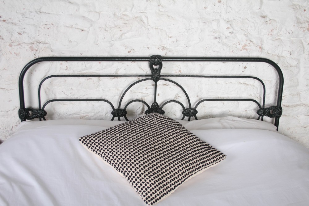An antique king-size black cast iron bed frame featuring a curved tubular headboard with central cast details and no footboard. View II