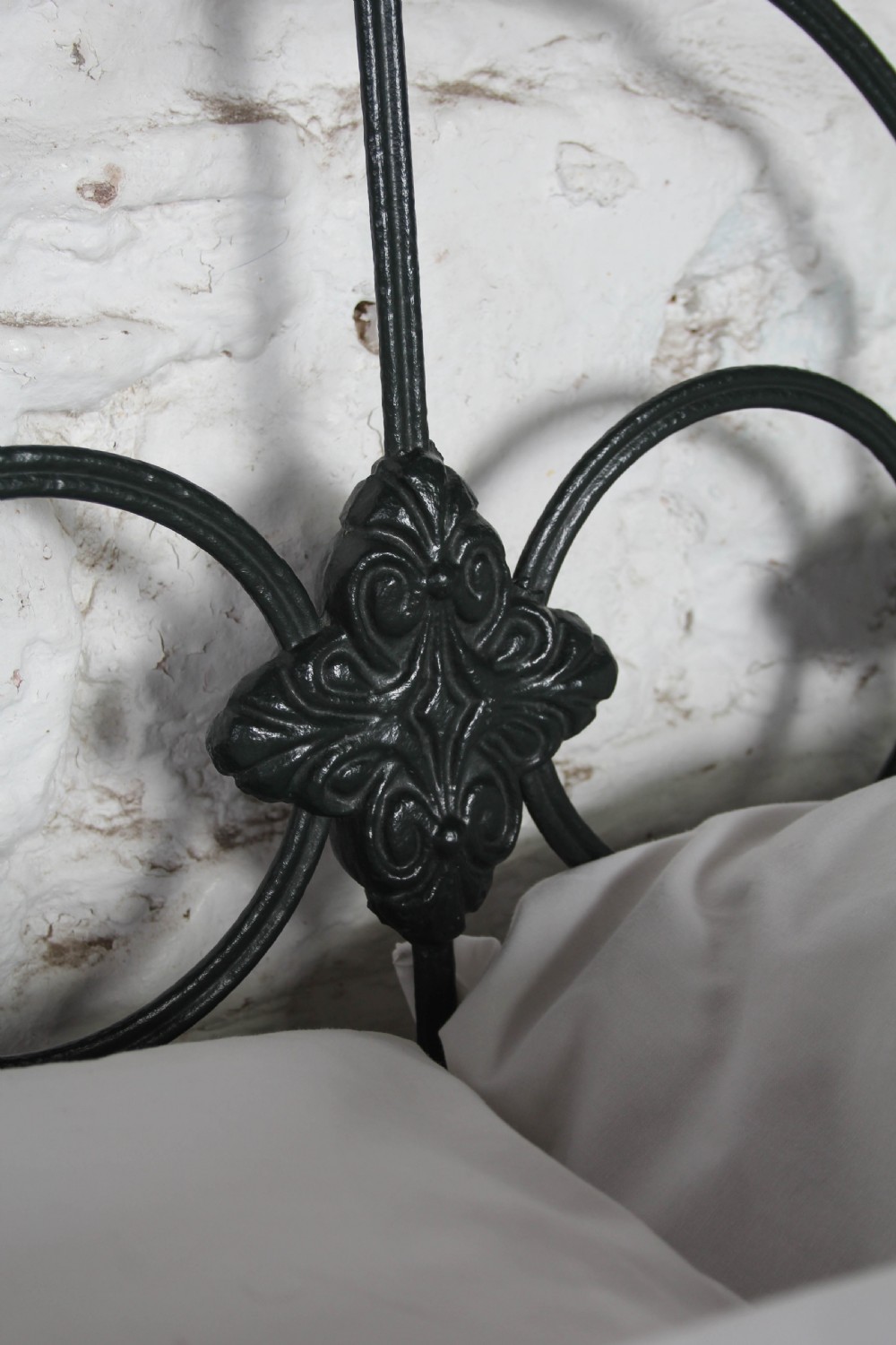 An antique king-size black cast iron bed frame featuring a curved tubular headboard with central cast details and no footboard. View III