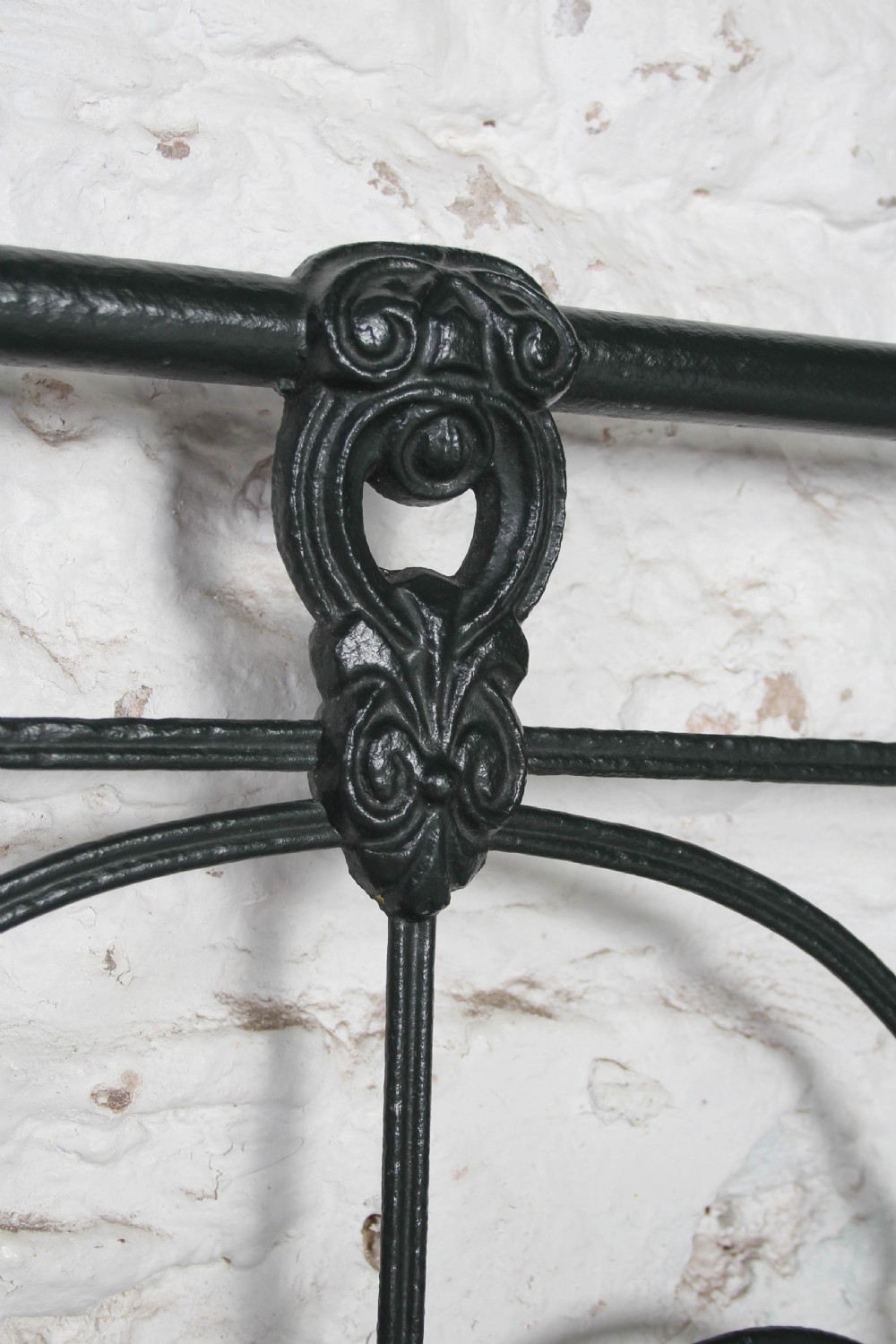 An antique king-size black cast iron bed frame featuring a curved tubular headboard with central cast details and no footboard. View IV