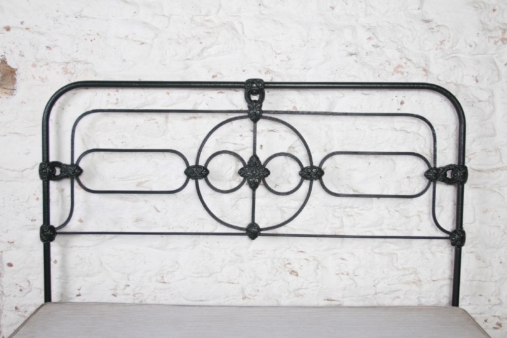 An antique king-size black cast iron bed frame featuring a curved tubular headboard with central cast details and no footboard. View VI