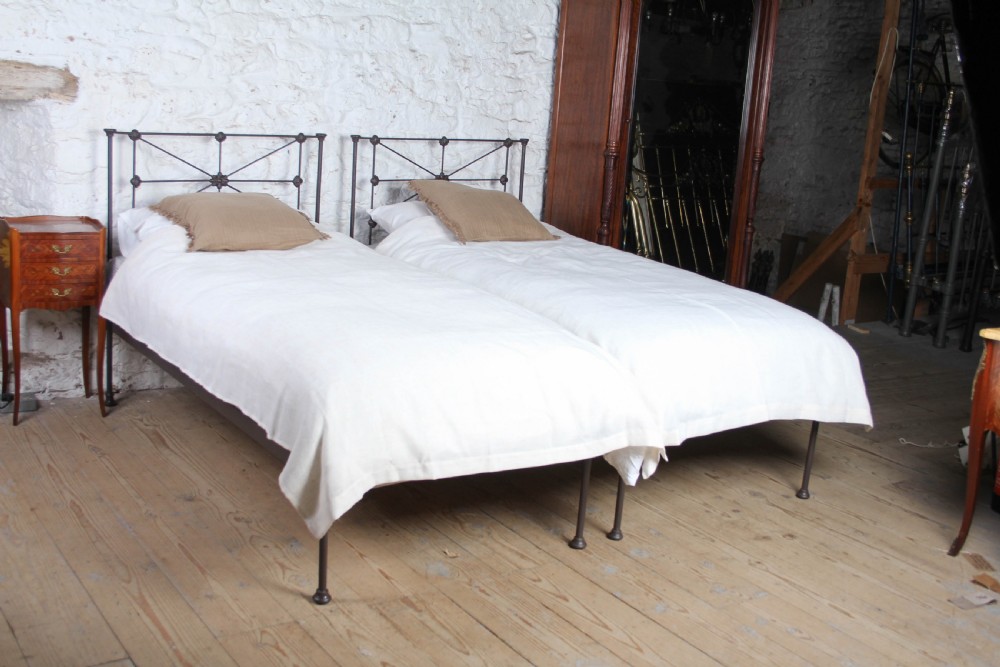 A pair of dark Victorian wrought iron single beds with geometric headboards and footless frames.