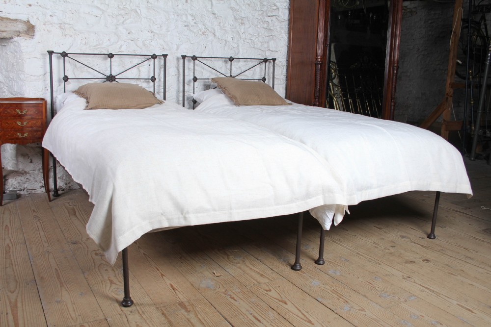 A pair of dark Victorian wrought iron single beds with geometric headboards and footless frames. View II