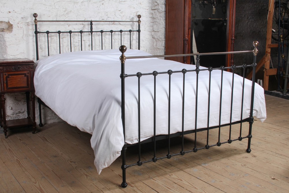 A Victorian black iron bedstead featuring vertical metal spindles, brass top rails, and round brass finials.