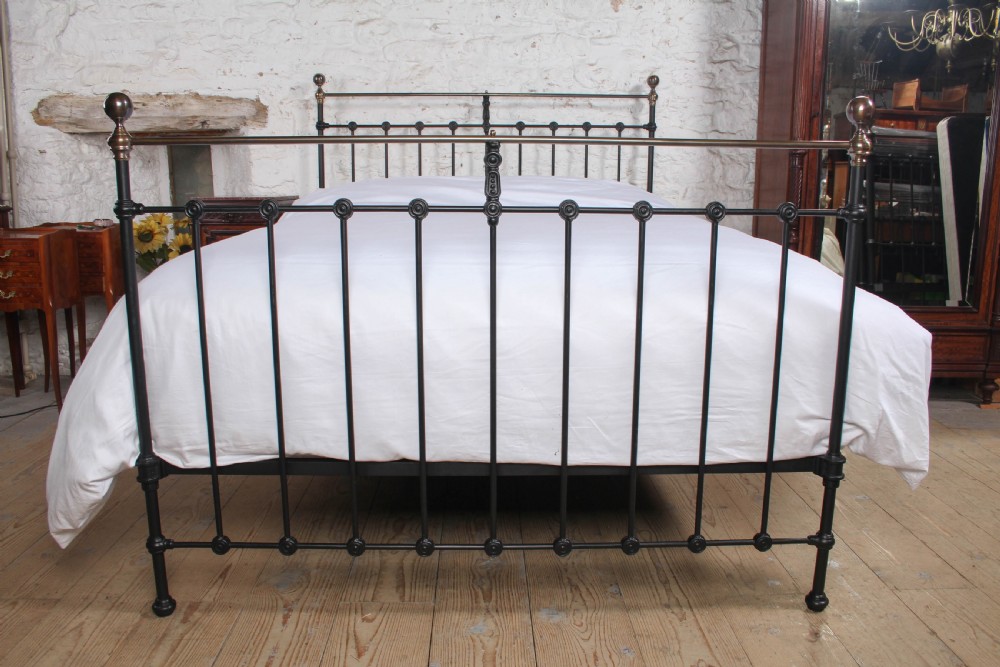 A Victorian black iron bedstead featuring vertical metal spindles, brass top rails, and round brass finials. View II