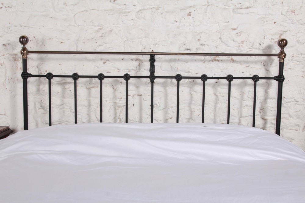 A Victorian black iron bedstead featuring vertical metal spindles, brass top rails, and round brass finials. View III