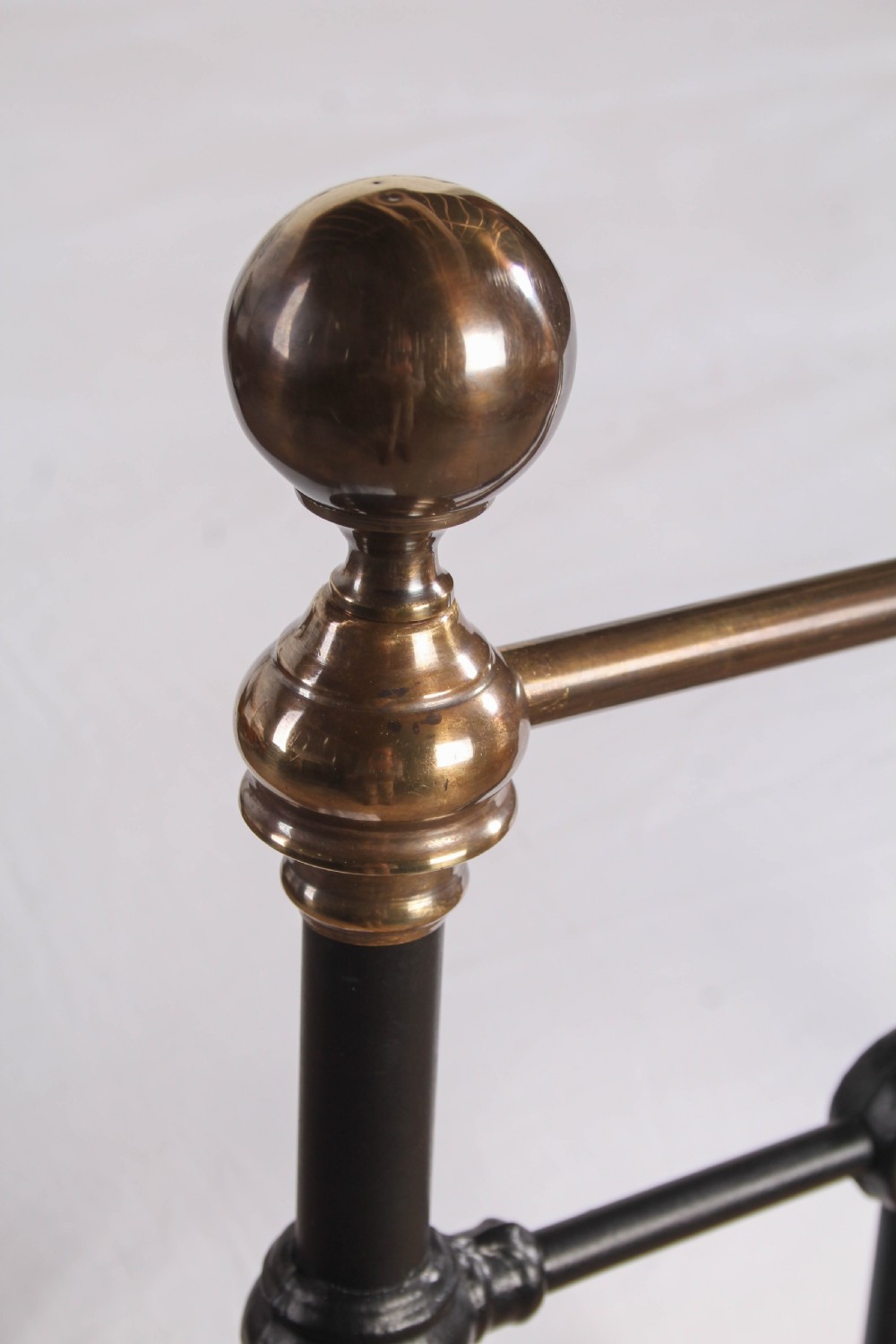 A Victorian black iron bedstead featuring vertical metal spindles, brass top rails, and round brass finials. View V