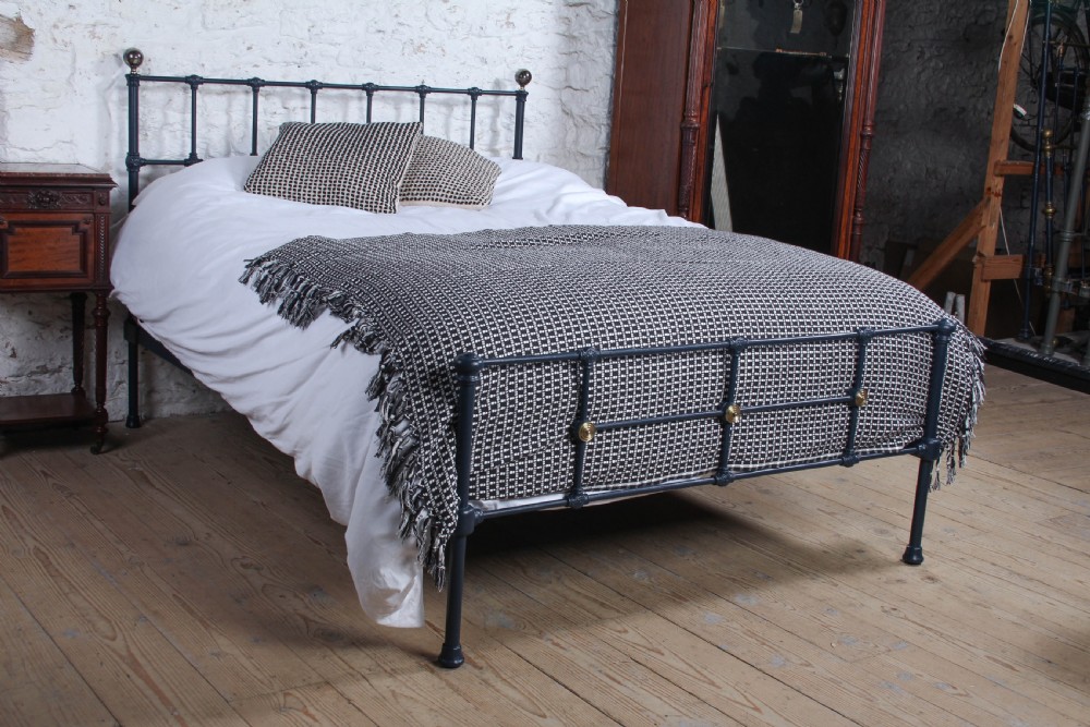 A Victorian style king size dark blue cast iron bedstead featuring decorative brass finials and a low footboard.