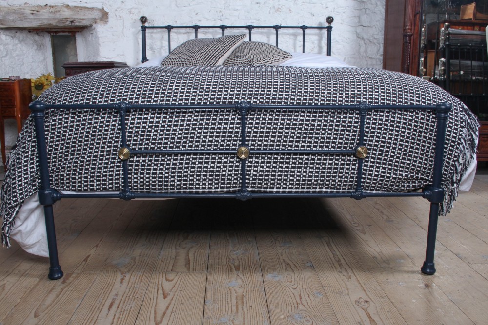 A Victorian style king size dark blue cast iron bedstead featuring decorative brass finials and a low footboard. View II