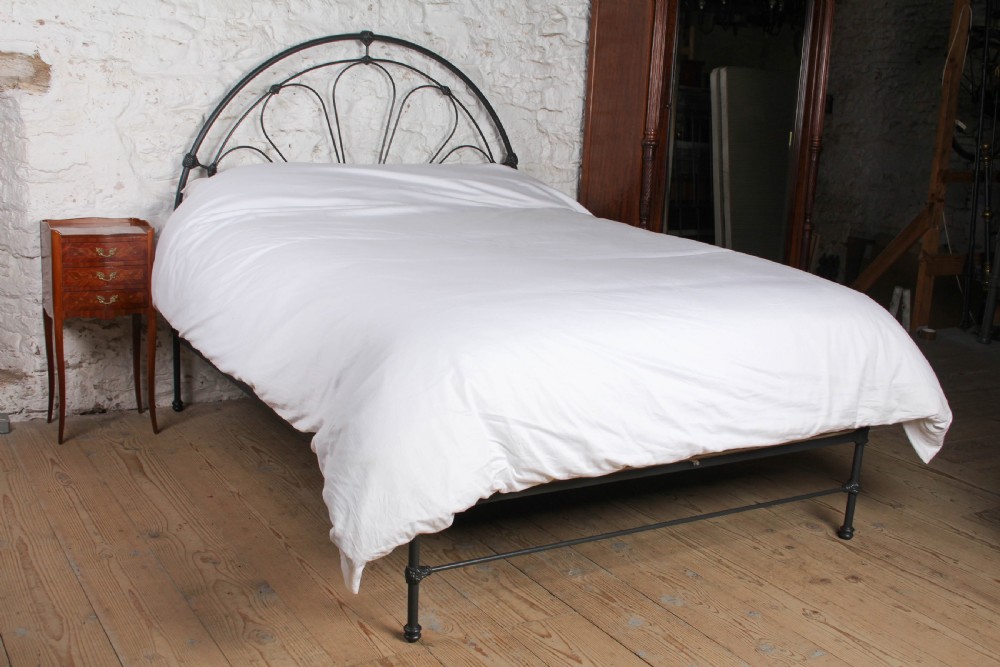 A Victorian black wrought iron king-size bed frame featuring an arched headboard with decorative scrollwork loops and a low footboard.