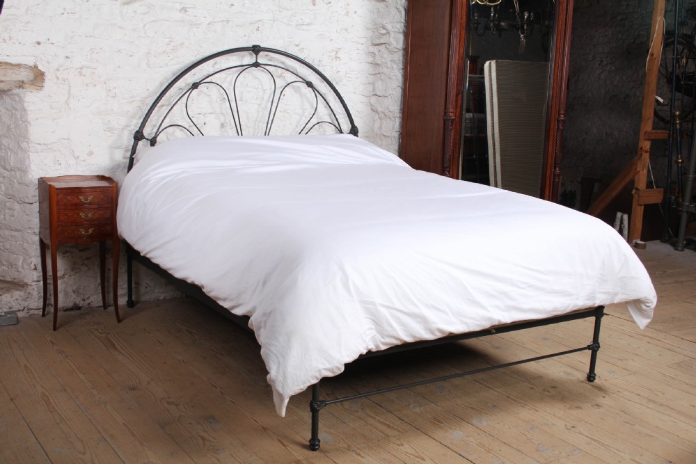 A Victorian black wrought iron king-size bed frame featuring an arched headboard with decorative scrollwork loops and a low footboard. View III
