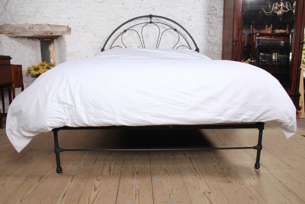 A Victorian black wrought iron king-size bed frame featuring an arched headboard with decorative scrollwork loops and a low footboard. View V