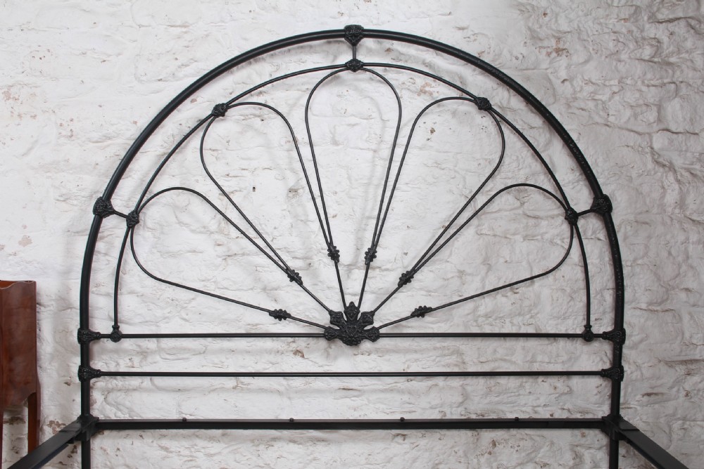 A Victorian black wrought iron king-size bed frame featuring an arched headboard with decorative scrollwork loops and a low footboard. View VI