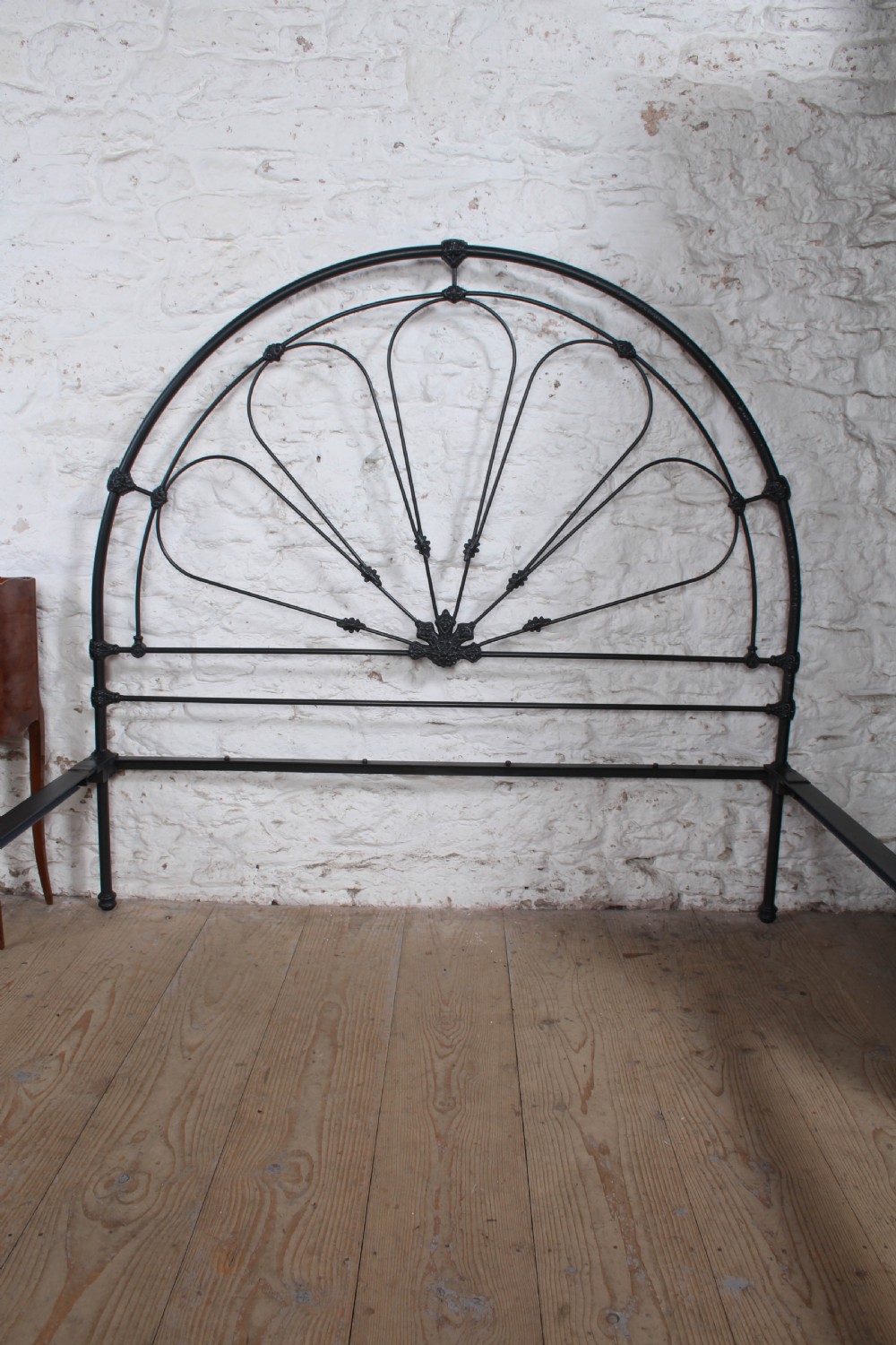 A Victorian black wrought iron king-size bed frame featuring an arched headboard with decorative scrollwork loops and a low footboard. View VII
