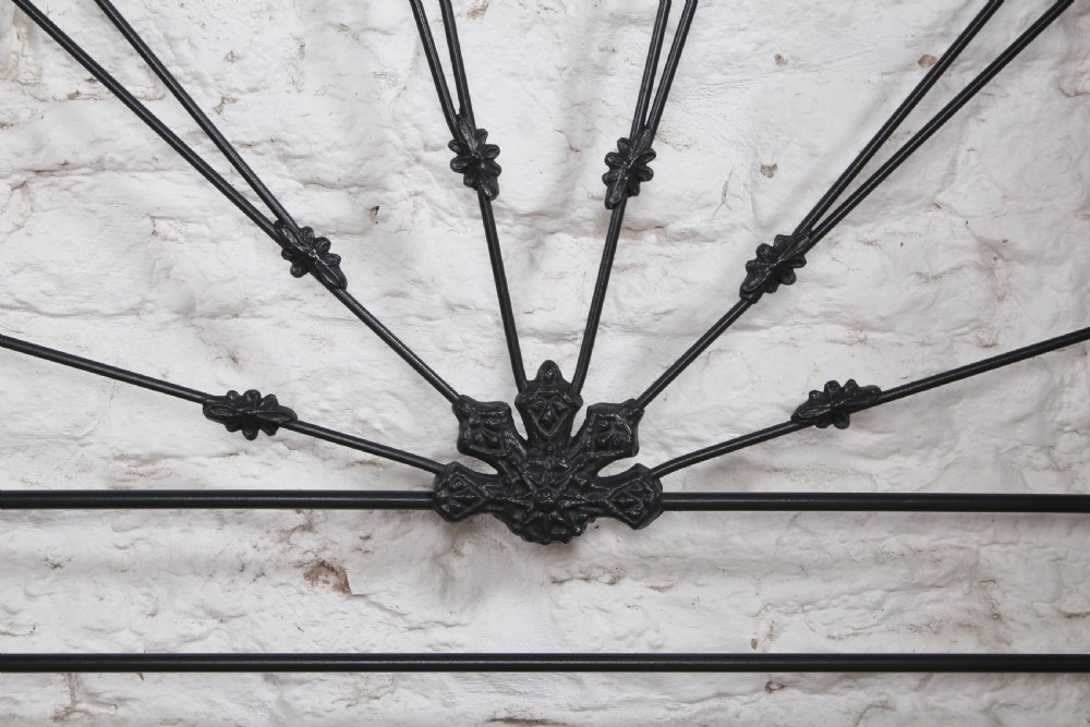 A Victorian black wrought iron king-size bed frame featuring an arched headboard with decorative scrollwork loops and a low footboard. View VIII