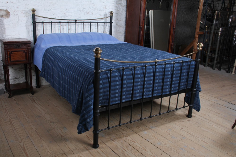 An Edwardian black iron and brass king-size bedstead featuring a curved dip rail and brass corner finials.