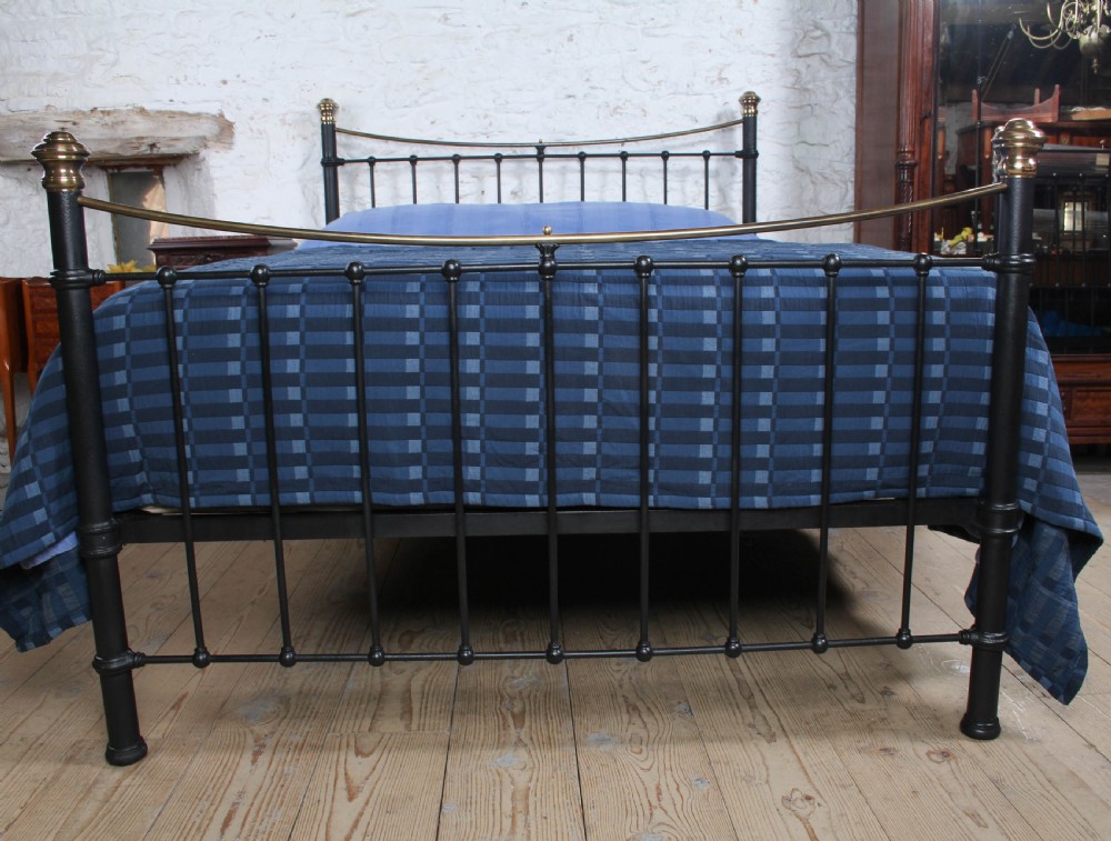 An Edwardian black iron and brass king-size bedstead featuring a curved dip rail and brass corner finials. View III